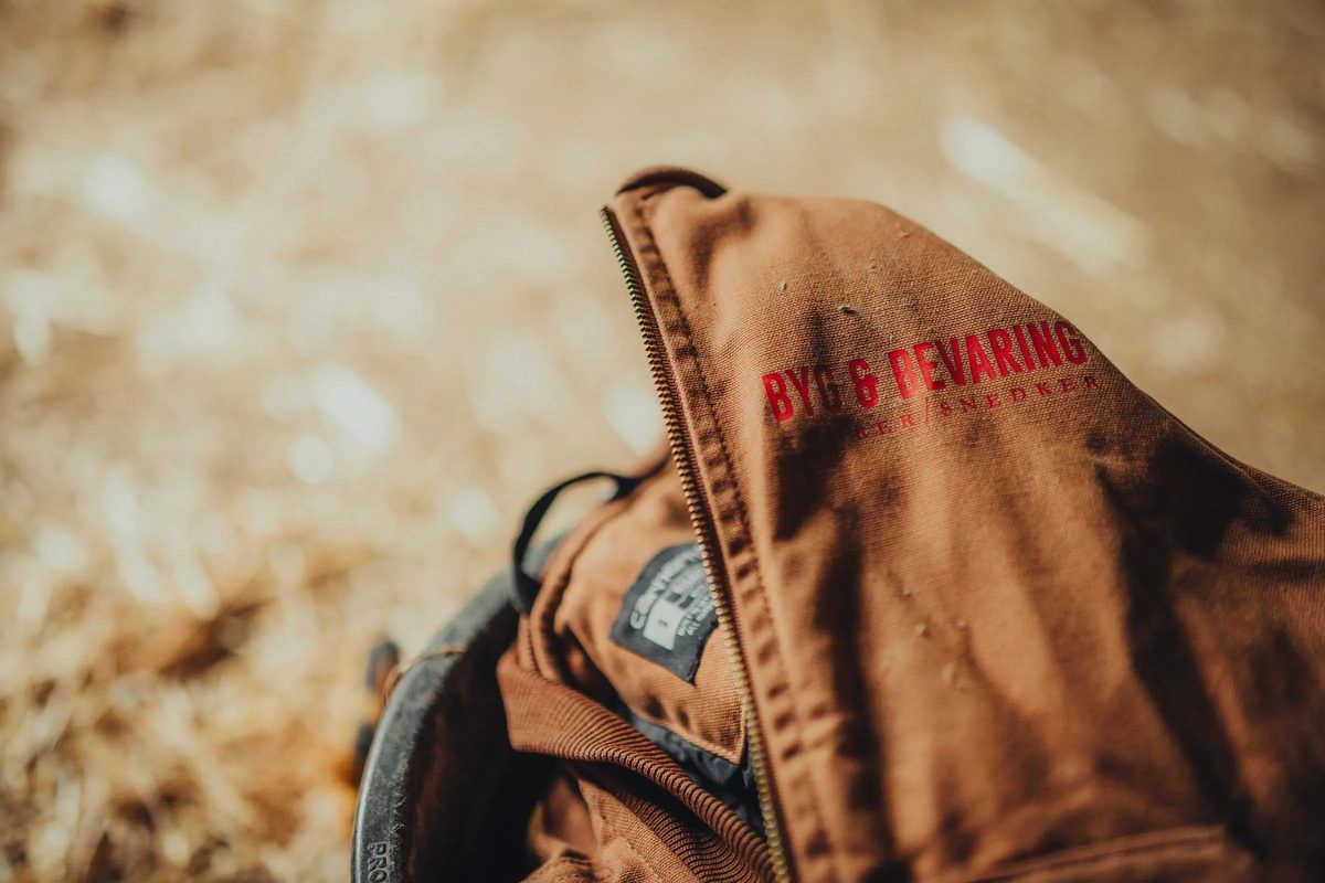Brun arbejdsjakke med Byg & Bevaring-logo.